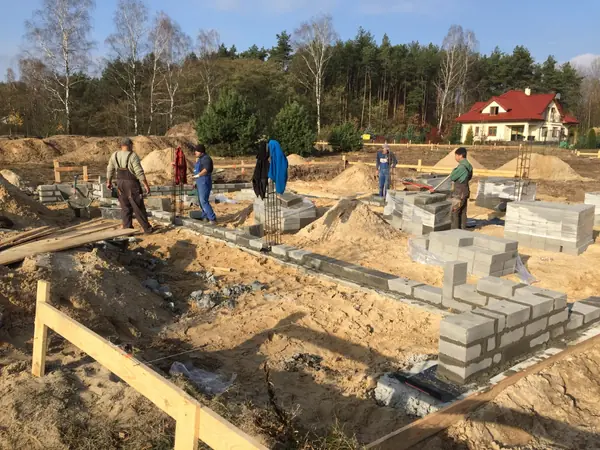 Wznoszenie ścian fundamentowych z bloczków betonowych — ekipa murarska pod nadzorem kierownika budowy, etap rozpoczęcia murów